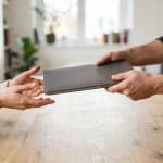 Person handing over a used laptop to a buyer across a table
