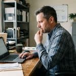 Small business owner looking concerned at a laptop in a back office