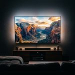 Large wall-mounted TV glowing with a vivid 4K cinematic scene in a dark cozy living room at night